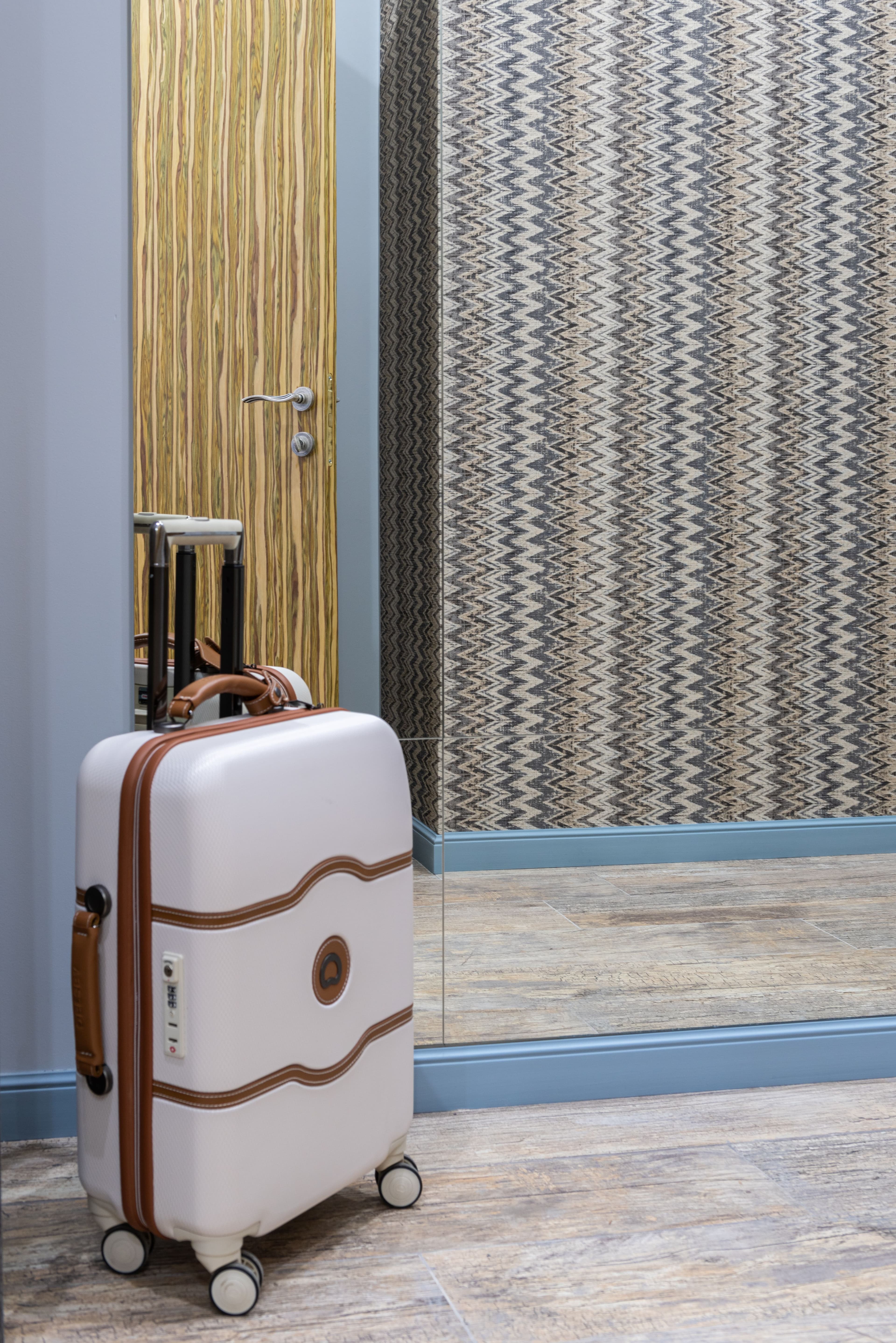 White suitcase with brown trim beside a mirror and wooden door; illustrative stock interior, not an Embrace development.
